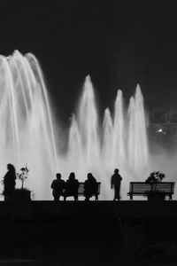 Silhouette people at fountain against sky at night