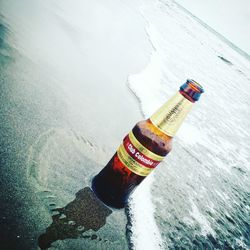 High angle view of hand holding bottle by sea during winter