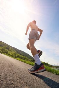 Rear view of man skateboarding on road against sky