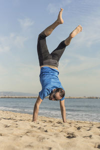 Man doing handstand on sand against sea at beach