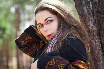 Close up young woman with shaman makeup leaning on tree portrait picture