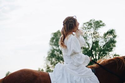 Rear view of woman riding dog against sky