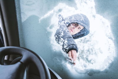 Low angle view of young man removing snow on windshield seen through car