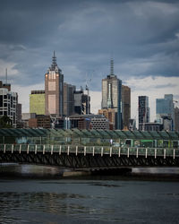 Modern buildings by river against sky in city