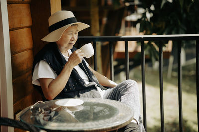 Side view of young woman drinking coffee while sitting in cage