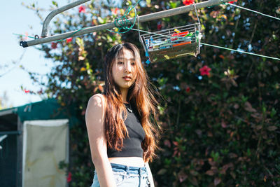 Low angle portrait of young woman against plants in backyard