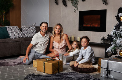 Family open christmas present gifts smiling, look at camera while sitting on  floor near xmas tree