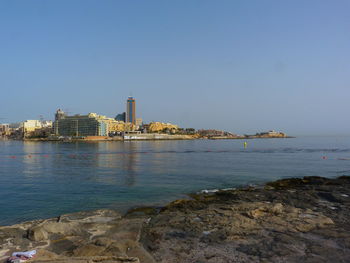 Sea by buildings against clear sky