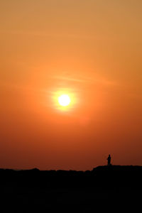 Silhouette man fishing against orange sky during sunset