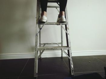 Low section of woman standing on step ladder against wall