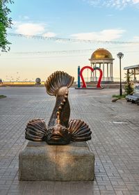 Sculpture on footpath by street against sky