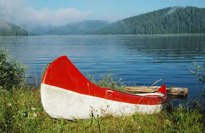 Red boat moored on shore by lake against sky