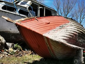 Abandoned boat moored on field by trees against sky