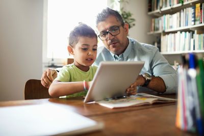 Father and son using digital tablet while studying at table