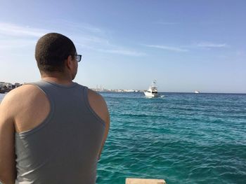 Rear view of man standing on boat in sea against sky