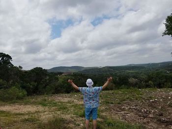 Rear view of man with arms outstretched standing against sky