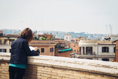 Rear view of woman standing on retaining wall against cityscape