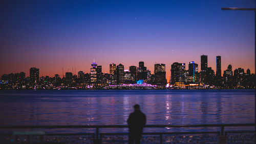 Illuminated city by river against sky at night