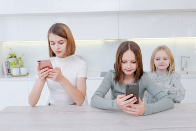 Smiling friends using mobile phone while sitting at home