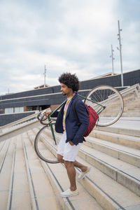 Stylish man carrying bicycle on stairs in the city