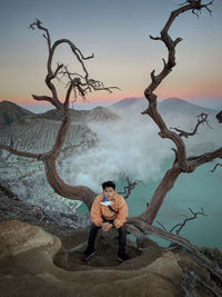 Full length of man sitting on tree against sky