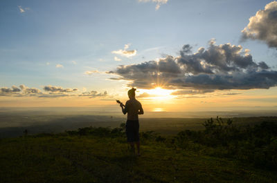 Silhouette man standing on field against sky during sunset