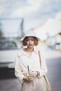 Portrait of young woman wearing hat standing on road