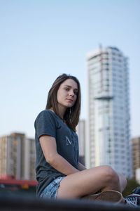 Low angle portrait of young woman sitting against clear sky