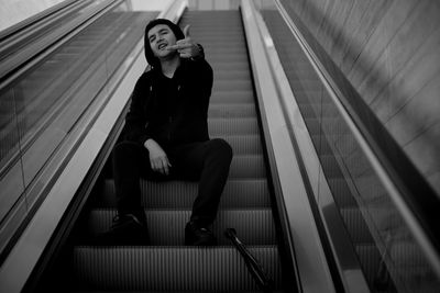 Portrait of man sitting on escalator while showing obscene gesture at subway station