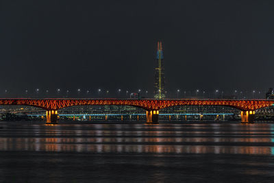 Illuminated bridge over river against sky in city at night