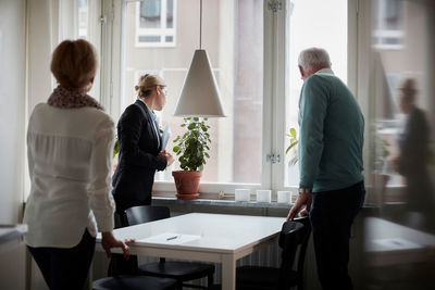 Senior couple and real estate agent looking through window at new home