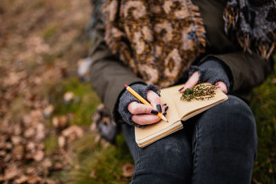 Midsection of woman writing in diary at forest