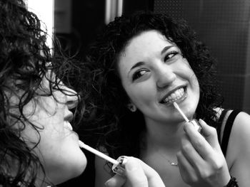 Close-up of young woman applying lip gloss reflecting on mirror