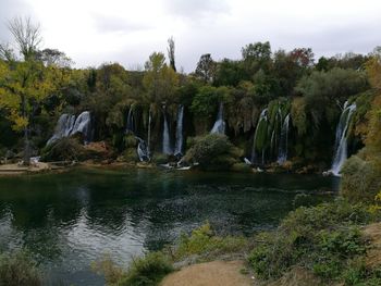 Scenic view of waterfall in front of trees against sky