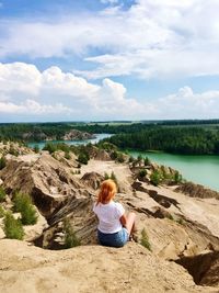 Rear view of woman sitting on rock against sky