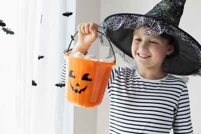 Halloween concept. a girl in a witch hat holds an orange pumpkin bucket with sweets.tricks or treats