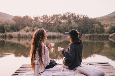 Woman sitting by lake against sky