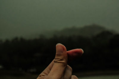 Close-up of human hand snapping against sky