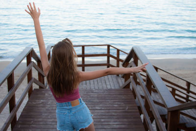 Rear view of woman walking on wooden railing against sea