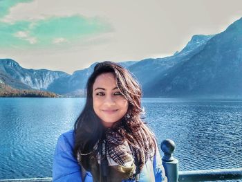 Portrait of smiling young woman standing on lake against mountains