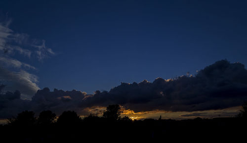 Low angle view of silhouette trees against blue sky