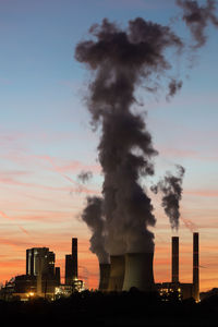 Smoke emitting from factory against sky during sunset