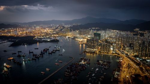 High angle view of victoria harbour by illuminated cityscape at night