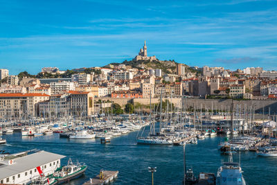 Sailboats moored on sea by buildings against sky in city