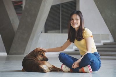 Portrait of smiling young woman sitting with dog on floor