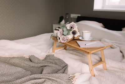 Romantic morning. wooden coffee table with flowers on bed with plaid, coffee cup, candles