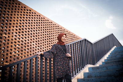 Low angle view of woman wearing hijab standing on staircase against sky