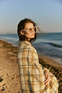 Portrait of young woman wearing sunglasses while standing at beach