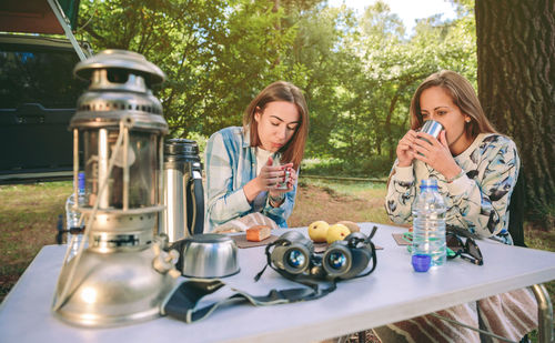 Friends drinking tea while sitting in forest