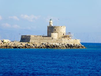 Scenic view of castle surrounded by calm blue sea against sky